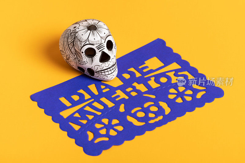 死亡的一天的陶器头骨(calavera)在蓝色papel picado在黄色背景，Dia de Muertos背景